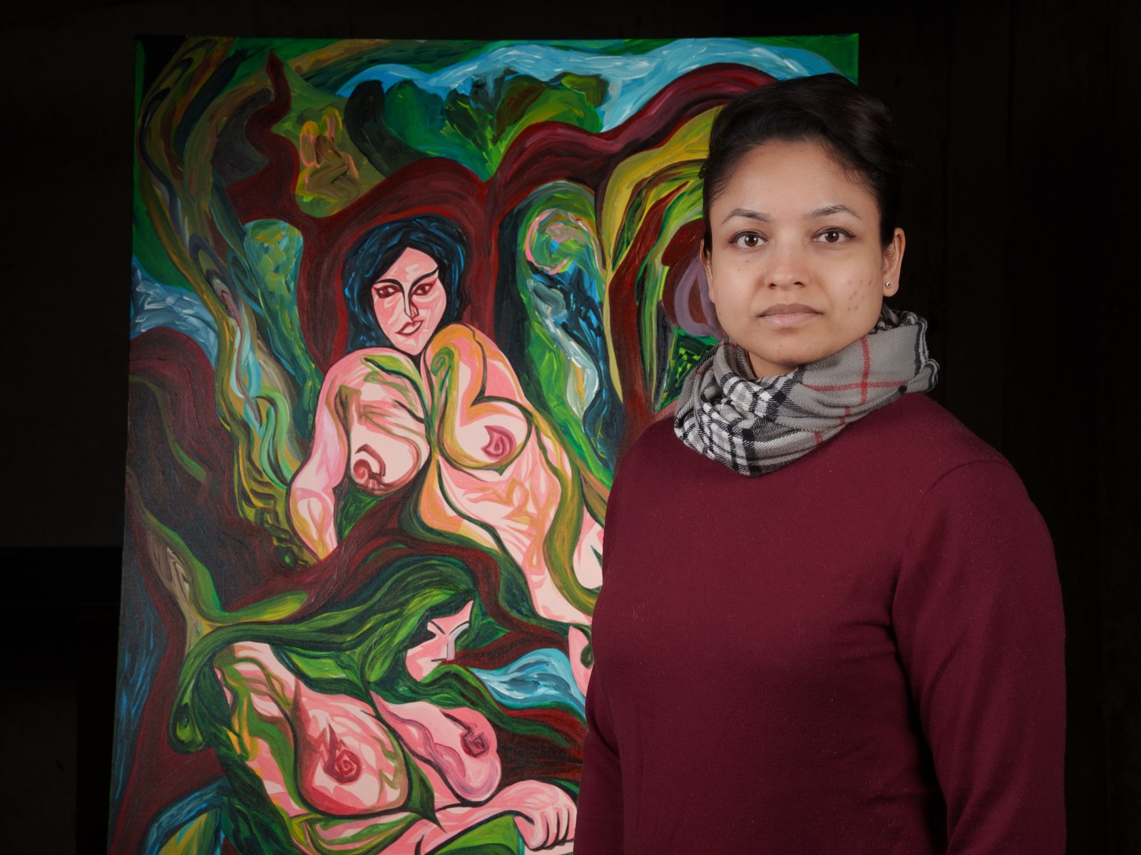 Payal Agarwal stands beside the canvas, her steady gaze mirroring the painted figure behind her. The Garden Consumes, 2026, by Payal Agarwal.