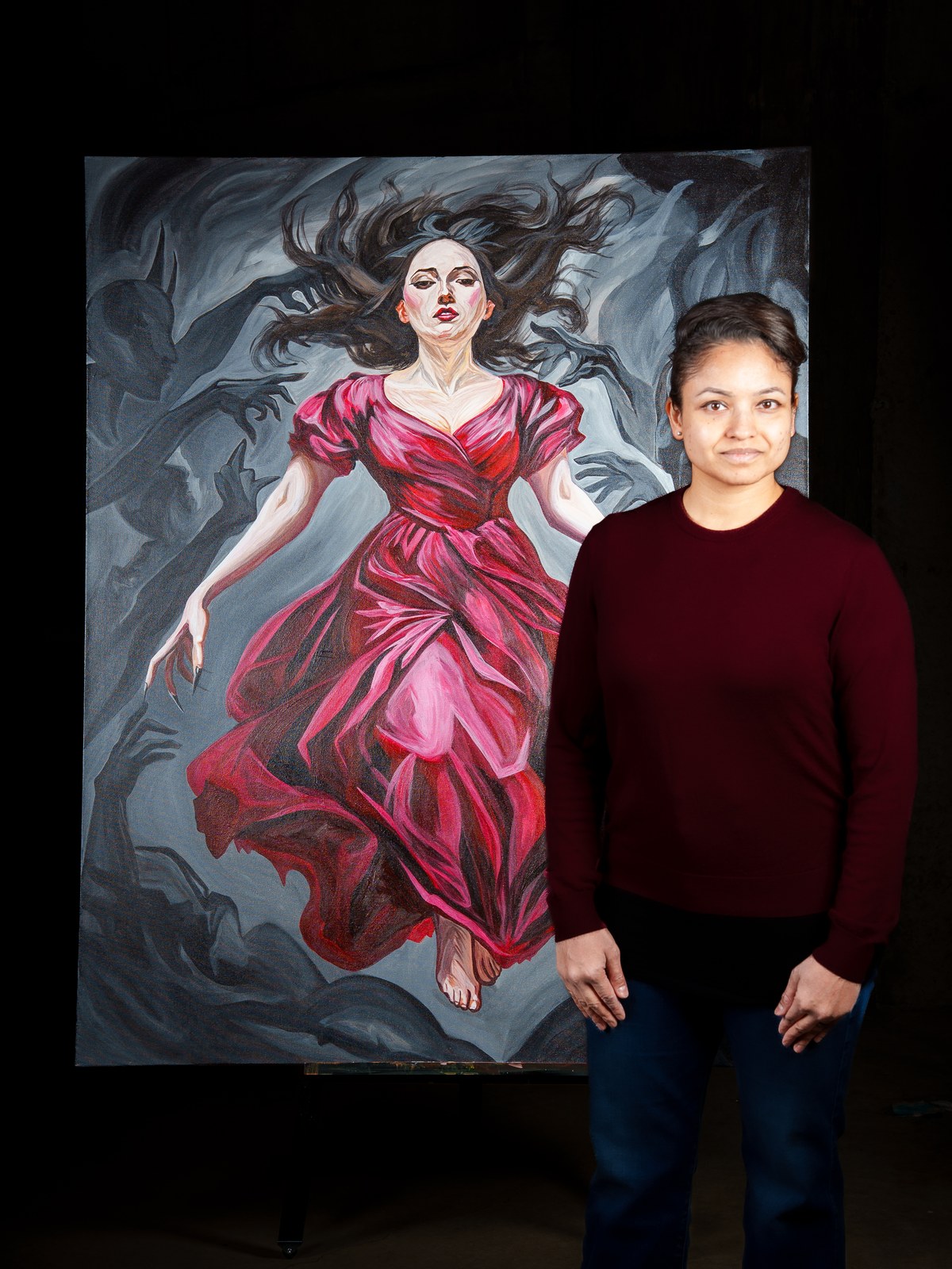 Payal Agarwal stands beside the finished canvas, her dark sweater echoing the painting's shadow palette. The Gravity of Touch, 2026, by Payal Agarwal.