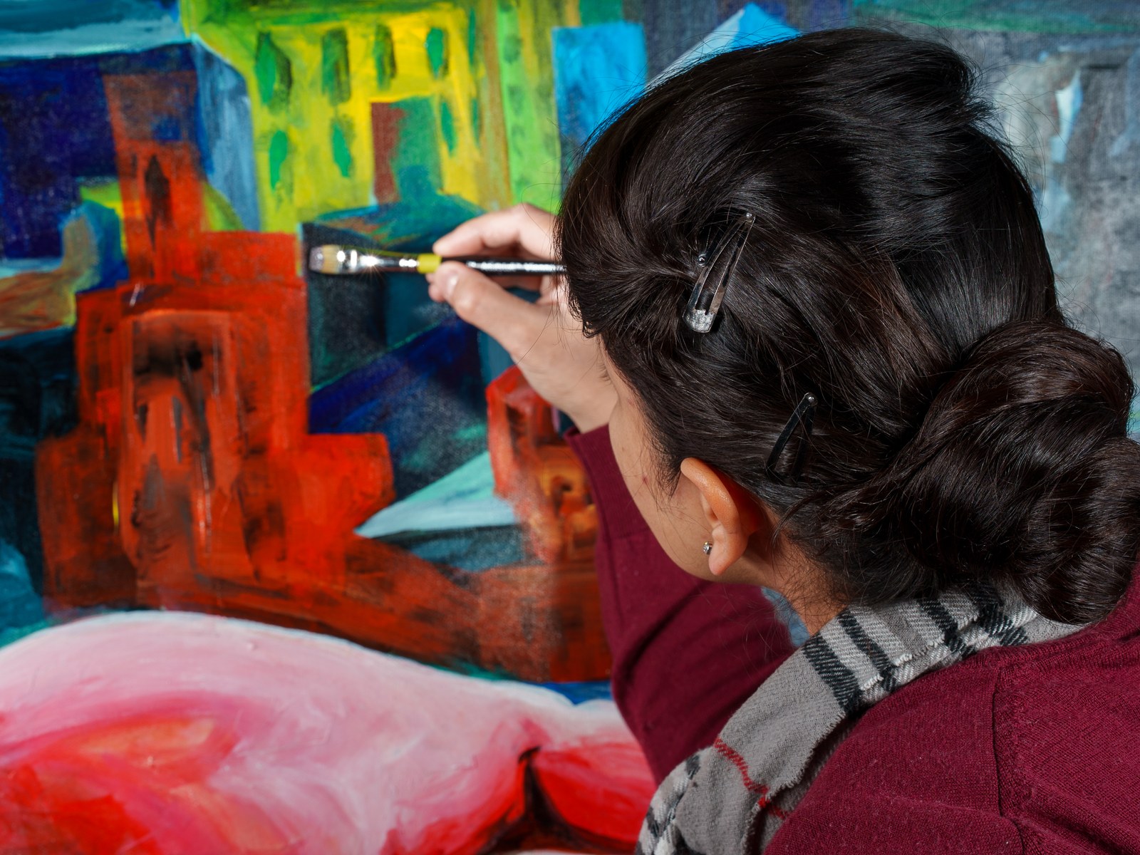 Payal Agarwal leans close to refine the painted skyline's vermilion blocks in mid-process. The Heat of Cold Distance, 2026, by Payal Agarwal.