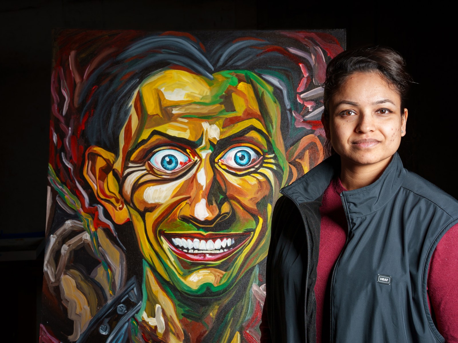 Payal Agarwal stands beside her grinning subject, calm against its red noise. The Insane Smile Longest, 2026, by Payal Agarwal.
